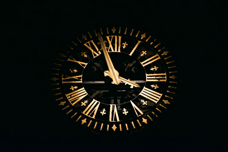 An ornate clock face with gold Roman numerals and gold hands, lit up against a black night sky.