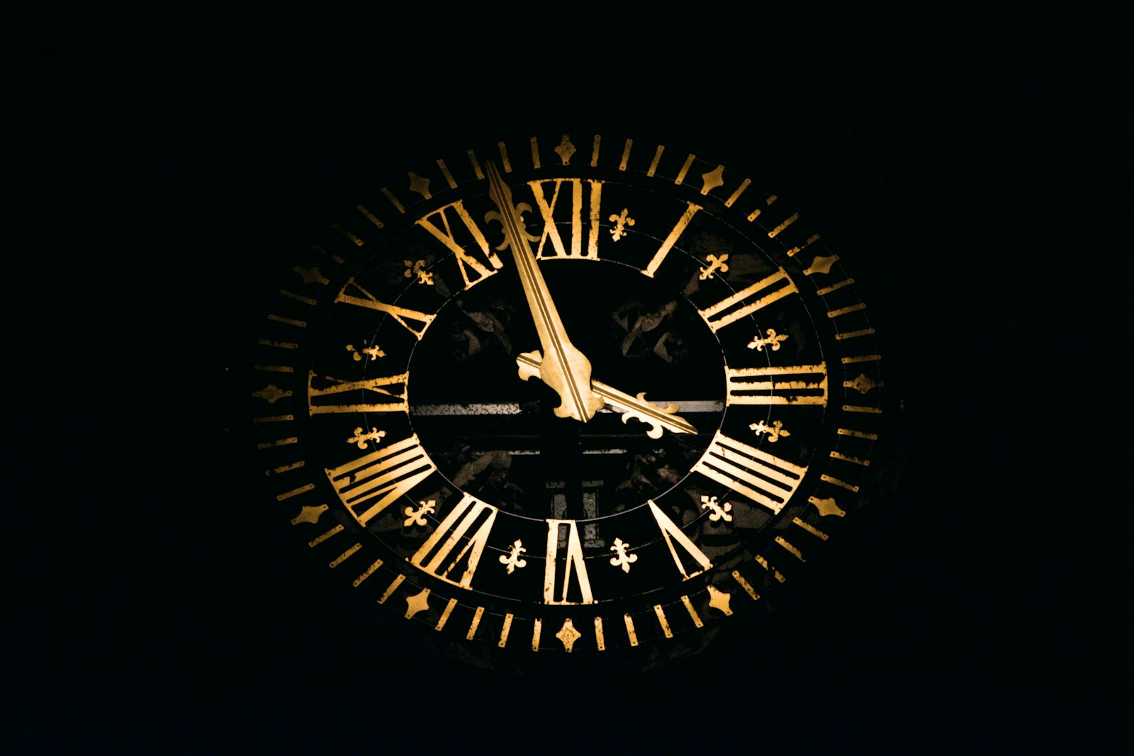 An ornate clock face with gold Roman numerals and gold hands, lit up against a black night sky.