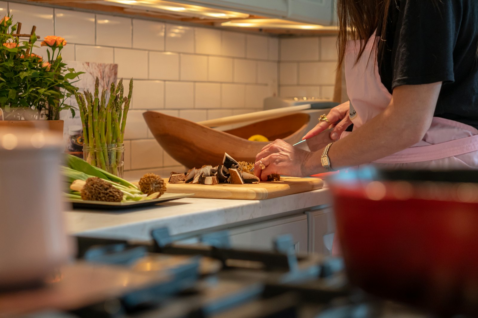 Someone prepping vegetables on a cutting board at a kitchen counter, flowers and a pot beside them.